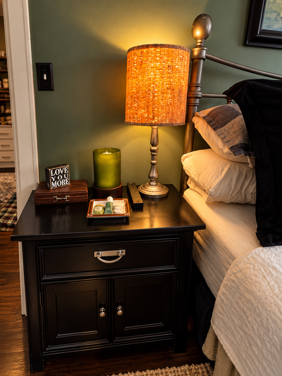 Guest bedside table with warm lamp, candle, power strip, and a tray of toiletries