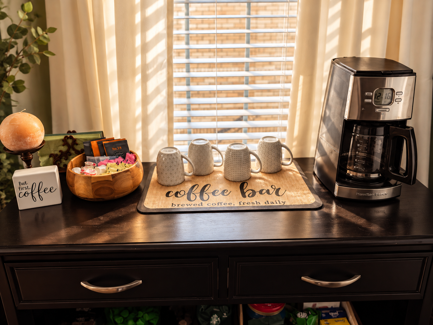Guest room coffee bar with coffee maker, mugs, tea, sweeteners, and coffee supplies beneath a window