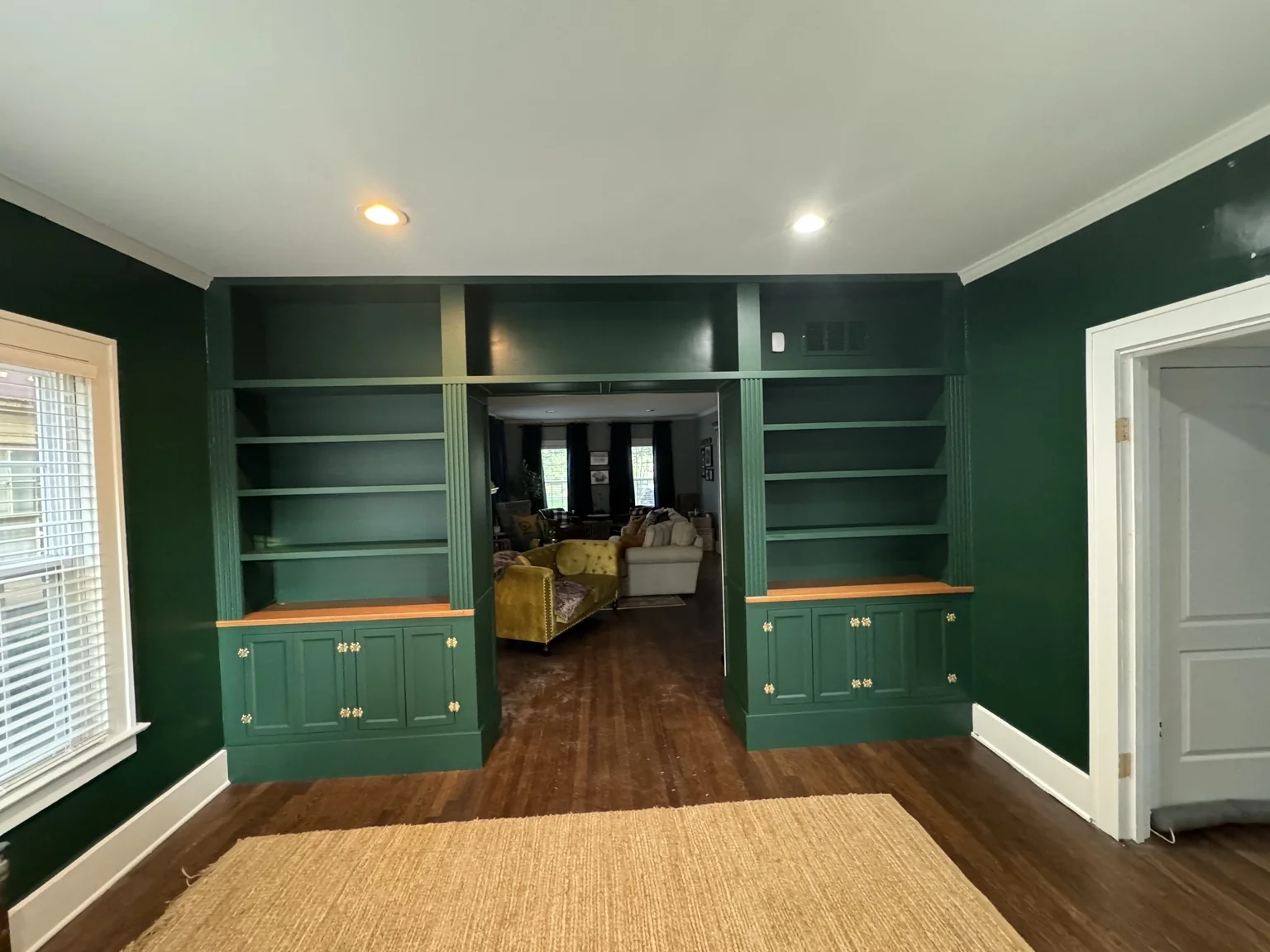 Completed green library built-ins with cabinet doors, brass hardware, and empty shelves