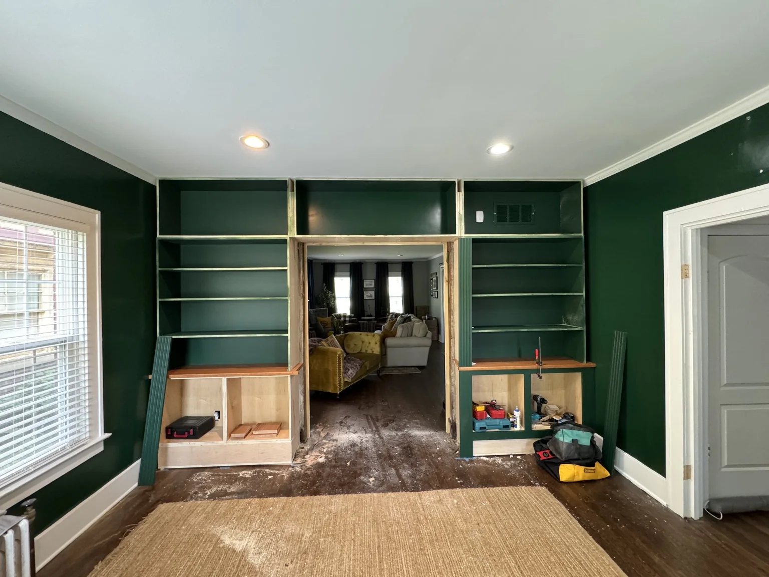 Custom green library bookcases installed around the wide passage with lower cabinets still unfinished
