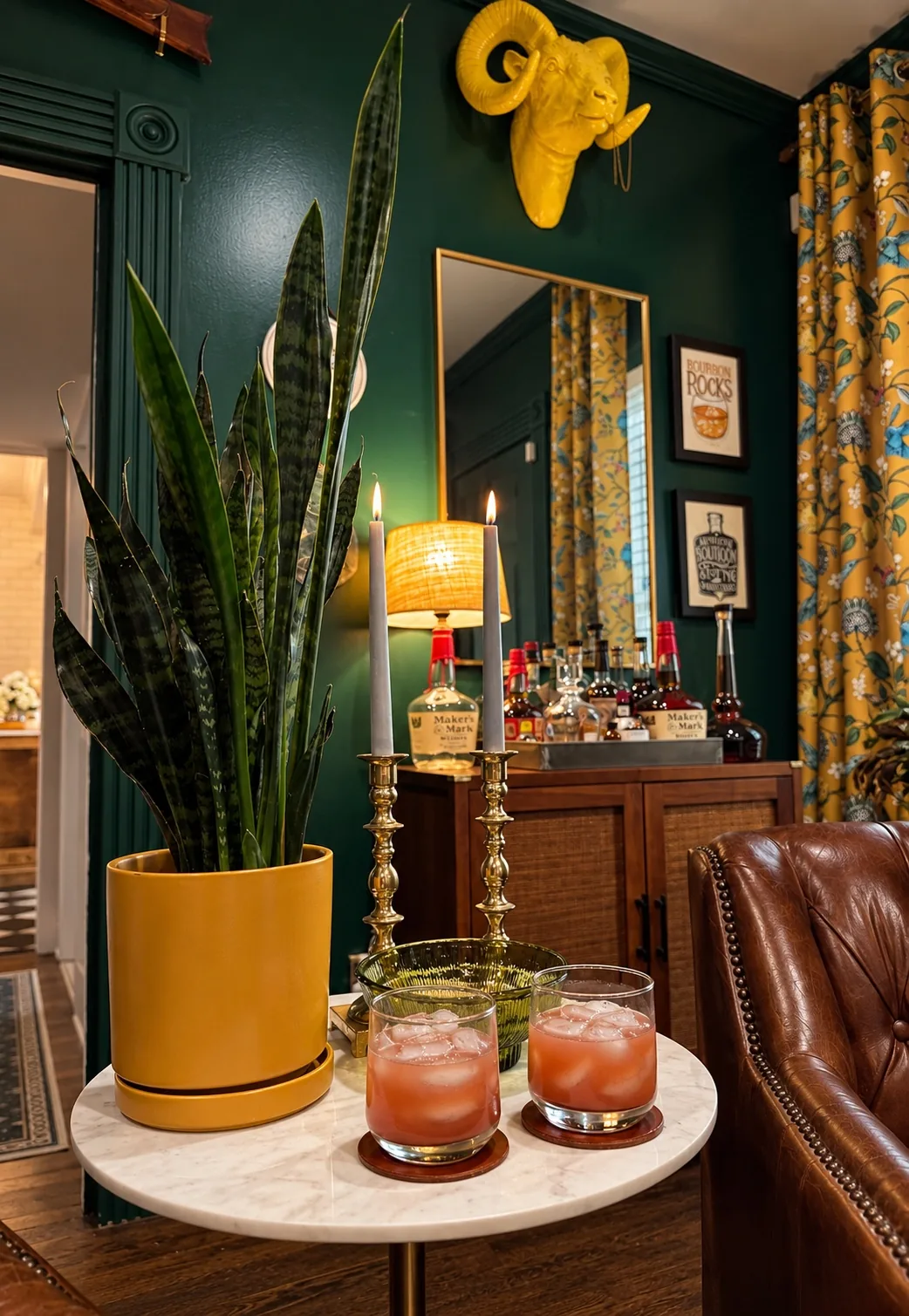 Cocktails on a marble table beside a leather chair in the deep-green library with brass candlesticks and yellow ram sculpture