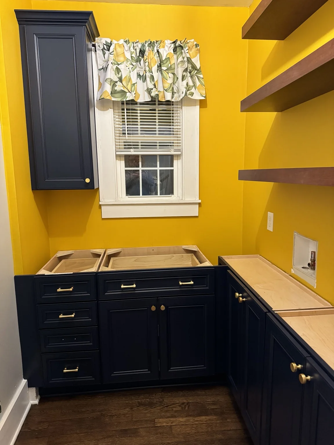 Dark pantry cabinets with brass hardware installed beneath bright yellow walls