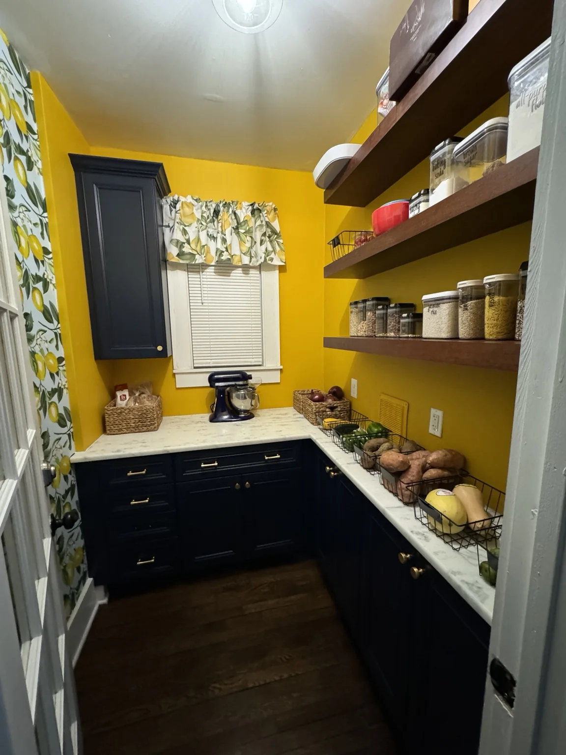 Finished pantry with floating wood shelves filled with dry goods and produce baskets along the counter