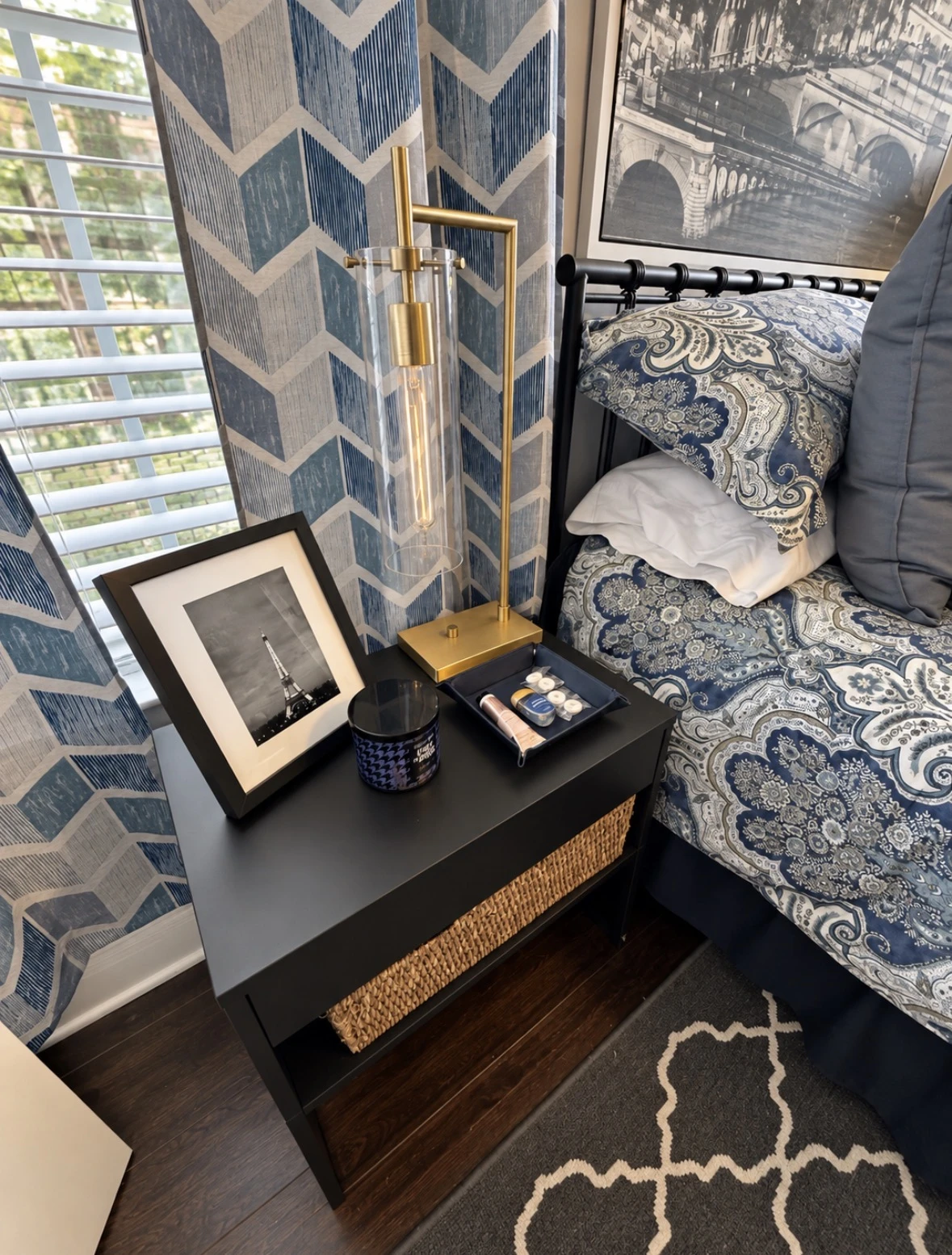 Brass and glass bedside lamp beside an Eiffel Tower photograph and a tray of toiletries