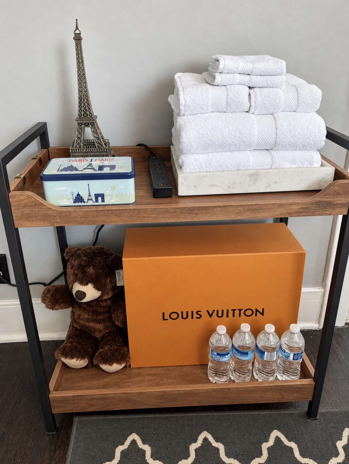Guest cart with white towels, an Eiffel Tower model, Paris tin, teddy bear and four water bottles