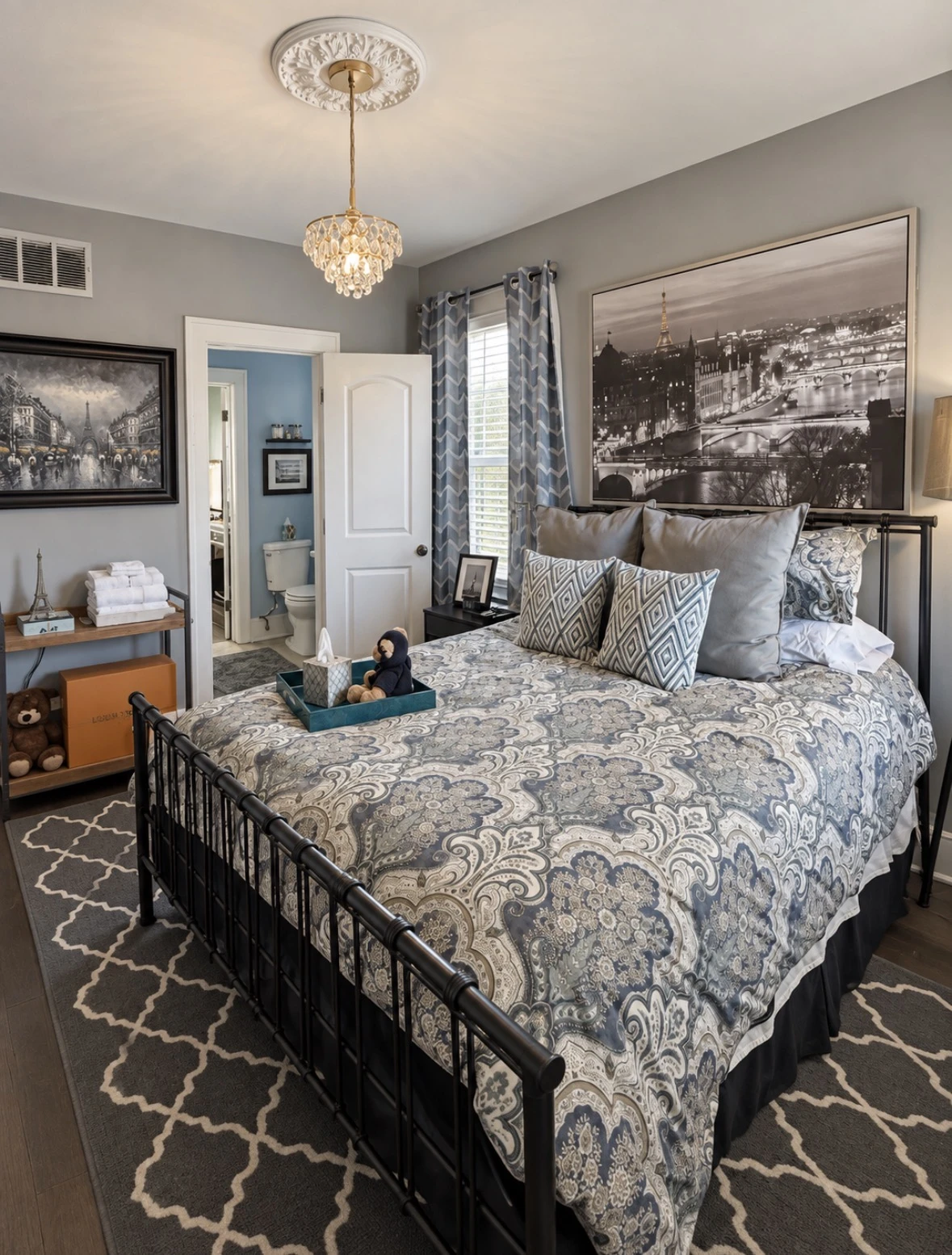 The Paris guest room with a black iron bed, blue-gray paisley bedding, Paris artwork and crystal chandelier