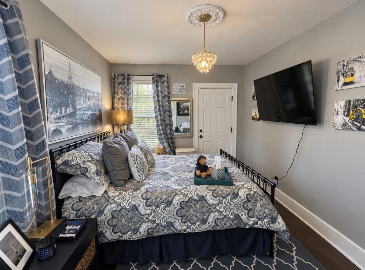 Wide view of The Paris with the bed, television, Paris artwork and patterned curtains