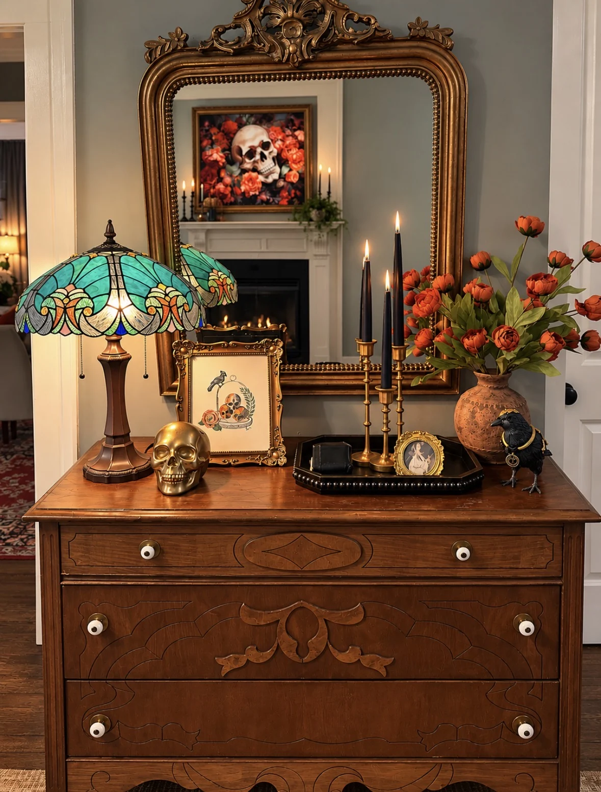 Antique dresser vignette with stained glass lamp, tapers, orange flowers, and raven figurine